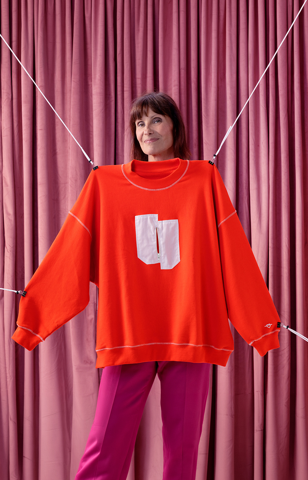 Femme portant le sweatshirt rouge de la campagne, devant un rideau rose